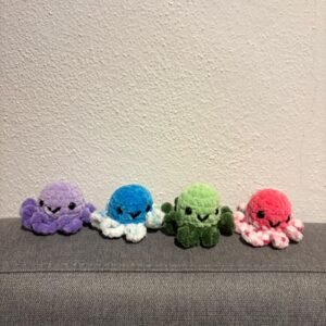 Vier kleine gehäkelte Oktopusse in lila, blau-weiß, grün und pink-weiß sitzen nebeneinander auf einem grauen Sofa.